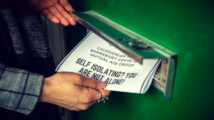 Image of someone inserting a flyer distributed by a mutual aid group in a door mail slot. 